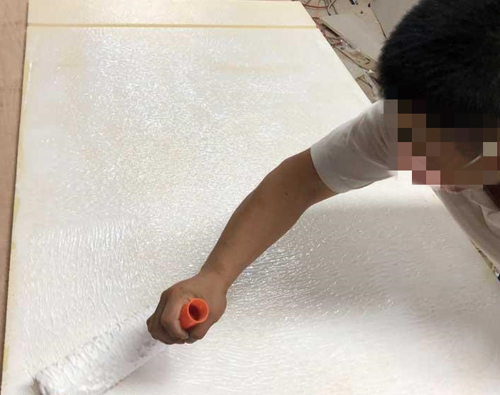 工人用滚筒在白色防撞软包板面滚涂胶粘剂，软包墙面安装施工现场实景